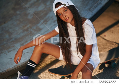 Taking a rest, sitting. Happy little girl with skateboard outdoors Taking a rest, sitting. Happy little girl with skateboard outdoors 128593222