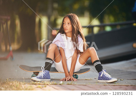 In the extreme sports park. Happy little girl with skateboard outdoors In the extreme sports park. Happy little girl with skateboard outdoors 128593231