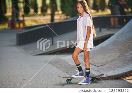 In the extreme sports park. Happy little girl with skateboard outdoors In the extreme sports park. Happy little girl with skateboard outdoors 128593232