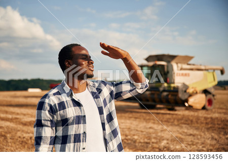 Machinery behind. Beautiful African American man is in the agricultural field Machinery behind. Beautiful African American man is in the agricultural field 128593456