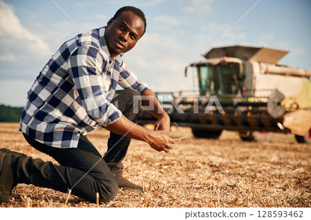 Machinery behind. Beautiful African American man is in the agricultural field Machinery behind. Beautiful African American man is in the agricultural field 128593462