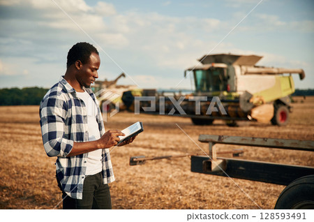 Standing, holding tablet. Beautiful African American man is in the agricultural field 128593491
