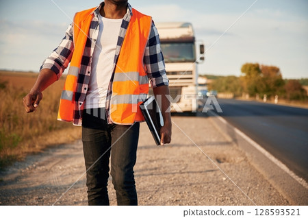 Front view. Black man is standing on the road with truck on it Front view. Black man is standing on the road with truck on it 128593521