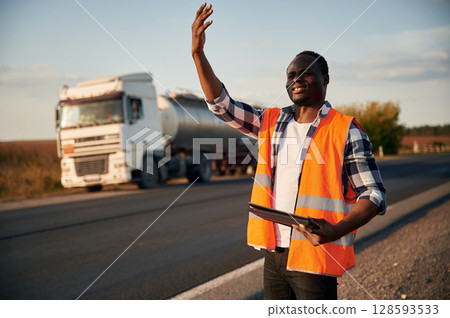 Showing the way. Black man is standing on the road with truck on it 128593533