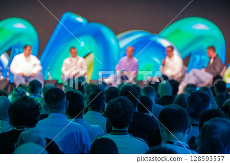 Audience Watching Panel Discussion in Conference Event with Colorful Backdrop 128593557