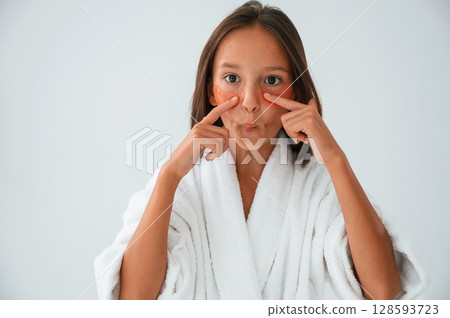 Orange colored eye patches on the face. Conception of beauty and self care. Young girl is in the studio Orange colored eye patches on the face. Conception of beauty and self care. Young girl is in the studio 128593723