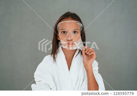Funny facial expression. Playing with mask. Conception of beauty. Young girl is in the studio 128593779