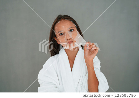 Funny facial expression. Playing with mask. Conception of beauty. Young girl is in the studio 128593780