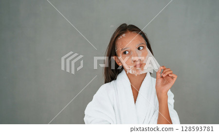 Funny facial expression. Playing with mask. Conception of beauty. Young girl is in the studio 128593781