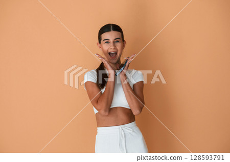Surprised, holding smartphone. Beautiful young woman in white clothes is standing indoors Surprised, holding smartphone. Beautiful young woman in white clothes is standing indoors 128593791