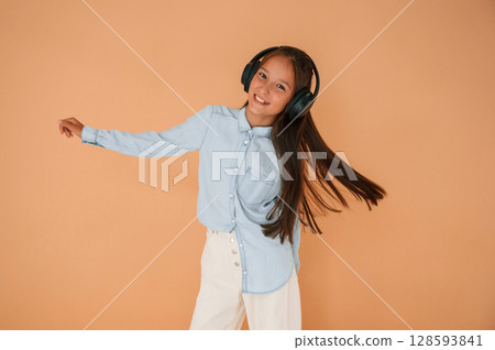 In headphones, positive energy. Cute young girl is in the studio against background In headphones, positive energy. Cute young girl is in the studio against background 128593841