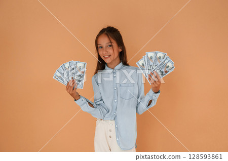 With bunch of currency, rich. Cute young girl is in the studio against background 128593861