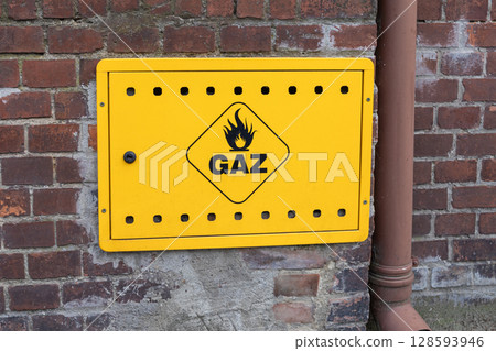 Yellow gas warning box with flame symbol and GAZ text mounted on an old brick wall, representing public utility and energy supply safety infrastructure 128593946