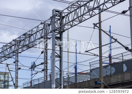 Intricate railway electrical catenary system with a complex network of metal structures and wires, supporting modern public transport infrastructure Intricate railway electrical catenary system with a complex network of metal structures and wires, supporting modern public transport infrastructure 128593972