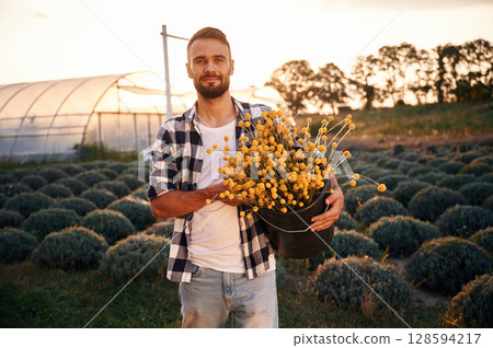 Succulent flowers of craspedia in hands. Young man on agricultural field near the greenhouse that is behind Succulent flowers of craspedia in hands. Young man on agricultural field near the greenhouse that is behind 128594217