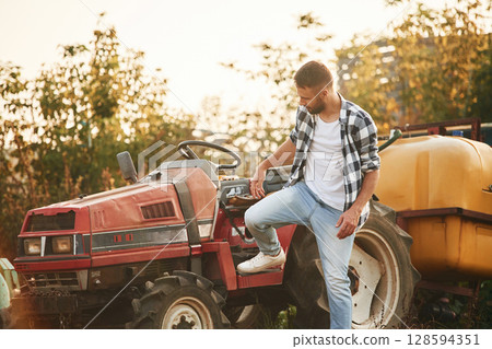 Farmer is casual clothes is standing near little tractor outdoors 128594351