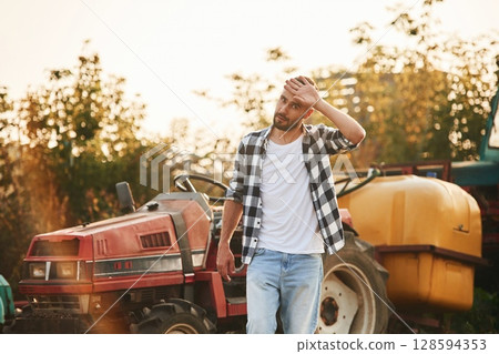 Farmer is casual clothes is standing near little tractor outdoors 128594353