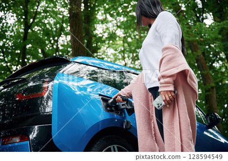 Woman is putting charger into the socket of electric automobile Woman is putting charger into the socket of electric automobile 128594549