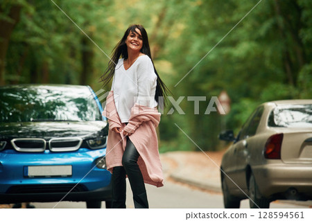 Cheerful beautiful woman is near blue car outdoors 128594561
