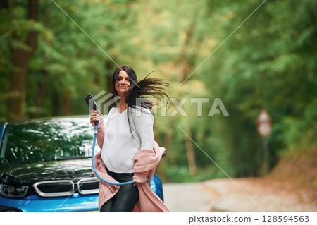 Cheerful beautiful woman is near blue car outdoors Cheerful beautiful woman is near blue car outdoors 128594563