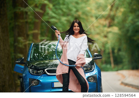 Cheerful beautiful woman is near blue car outdoors 128594564