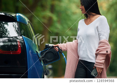 Woman is putting charger into the socket of electric automobile 128594568