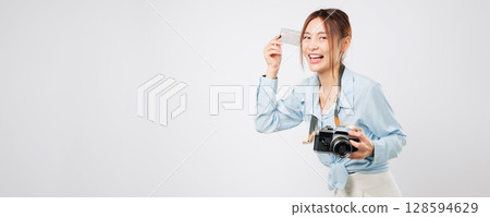 Travel moment captured as happy Asian woman shops for travel items. Holding a vintage photo camera and card bank, she smiles at the journey ahead. tourism and vacation isolated studio white background Travel moment captured as happy Asian woman shops for travel items. Holding a vintage photo camera and card bank, she smiles at the journey ahead. tourism and vacation isolated studio white background 128594629