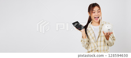 Excited woman manages saving plan by checking numbers on calculator, then reviewing on second calculator, using piggybank and tax strategy for smart finance. isolated studio white background Excited woman manages saving plan by checking numbers on calculator, then reviewing on second calculator, using piggybank and tax strategy for smart finance. isolated studio white background 128594630