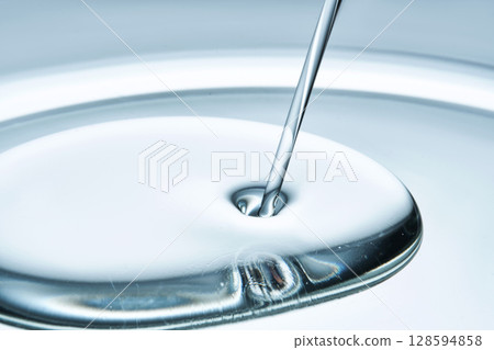 The beautiful texture of the facial oil pouring and gathering into a drop in blue tones. The beautiful texture of the facial oil pouring and gathering into a drop in blue tones. 128594858