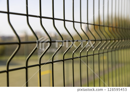 fence against a blue sky background, a small thin fence dividing the territory against a cloudless sky background 128595453