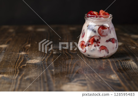 yogurt with cherry flavor and berry slices, glass jar with cherry yogurt with fresh red cherries close up, side view, an empty table 128595483