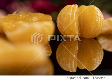 the reflection of a white orange citrus tangerine in a black mirror surface, a beautiful peeled and juicy tangerine on a black mirror 128595499