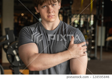 Athlete or young man standing with pain in shoulder at gym. Arm, inflammation or exercise with discomfort at fitness center. Close up. Athlete or young man standing with pain in shoulder at gym. Arm, inflammation or exercise with discomfort at fitness center. Close up. 128595846