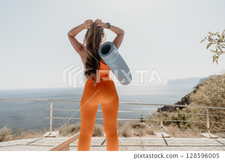 Woman in Orange Sportswear with Yoga Mat on a Clifftop Woman in Orange Sportswear with Yoga Mat on a Clifftop 128596005