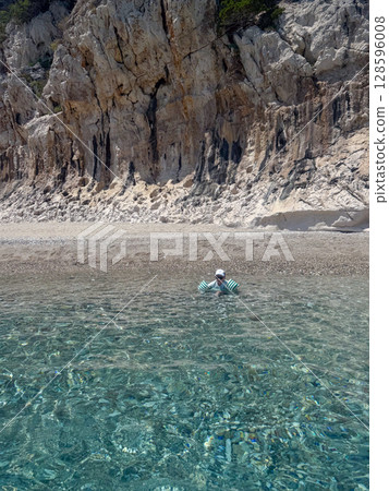 Boy with floaties enjoying transparent sea water near stony beach and high cliffs in Sardinia, Italy. Cala luna Boy with floaties enjoying transparent sea water near stony beach and high cliffs in Sardinia, Italy. Cala luna 128596008