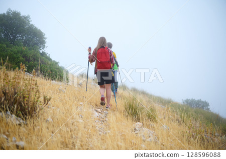 Two Hikers Trekking Through a Misty Hillside with Yellow Grass Two Hikers Trekking Through a Misty Hillside with Yellow Grass 128596088