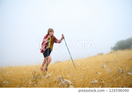 Young Woman Hiking in a Dry Grass Landscape on a Foggy Morning with Walking Poles 128596090
