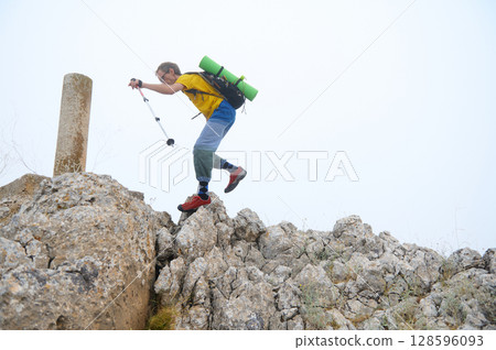 Adventurous Hiker Scaling Rocky Outcrop with Gear in Bright Daylight 128596093