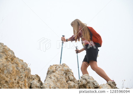 Young Female Hiker Scaling Rocks with Poles in Mountain Landscape on Misty Day Young Female Hiker Scaling Rocks with Poles in Mountain Landscape on Misty Day 128596094