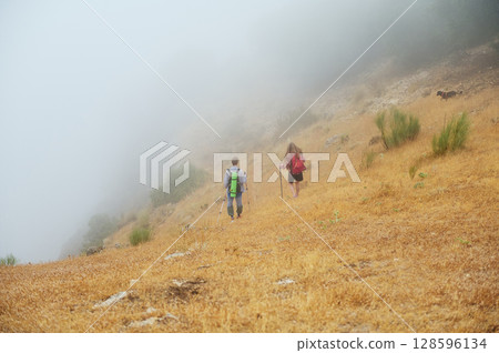 Couple Hiking on a Foggy Mountain Trail Through Dry Grassland and Mist Couple Hiking on a Foggy Mountain Trail Through Dry Grassland and Mist 128596134