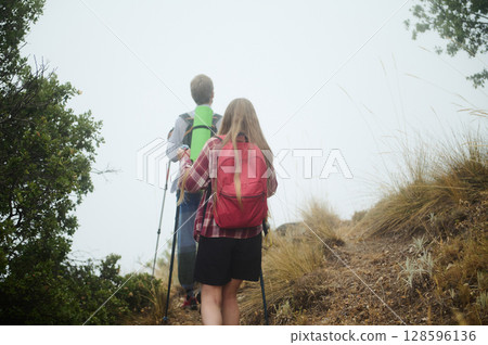 Couple Hiking Through Foggy Mountain Path Surrounded by Grass and Trees Couple Hiking Through Foggy Mountain Path Surrounded by Grass and Trees 128596136