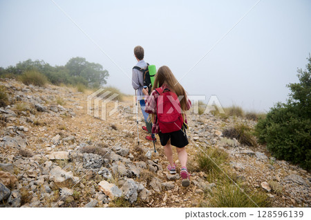 Hikers Traversing a Rocky Path in a Foggy Mountain Landscape 128596139