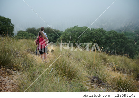 Two Hikers Exploring a Scenic Mountain Trail Surrounded by Lush Greenery in Misty Conditions 128596142