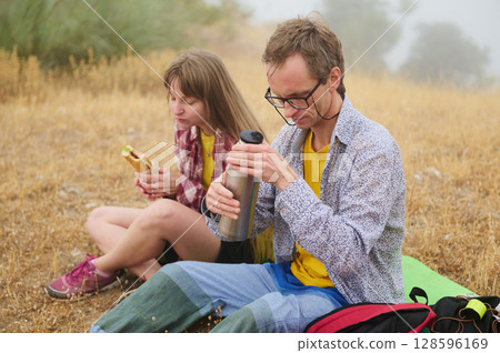 Couple Enjoying A Picnic Break in Nature While Hiking Through a Grassland Area Couple Enjoying A Picnic Break in Nature While Hiking Through a Grassland Area 128596169