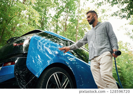 Young man is putting charger into the socket of electric automobile Young man is putting charger into the socket of electric automobile 128596720