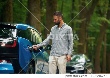 Young man is putting charger into the socket of electric automobile 128596748