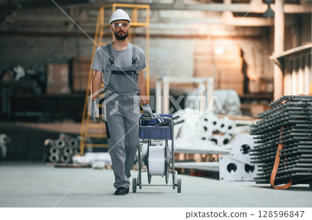 Front view, walking forward. Young factory worker in grey uniform 128596847