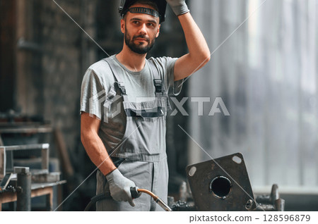 Welder man in safety helmet. Young factory worker in grey uniform Welder man in safety helmet. Young factory worker in grey uniform 128596879