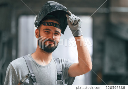 Welder man in safety helmet. Young factory worker in grey uniform Welder man in safety helmet. Young factory worker in grey uniform 128596886