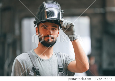Welder man in safety helmet. Young factory worker in grey uniform 128596887